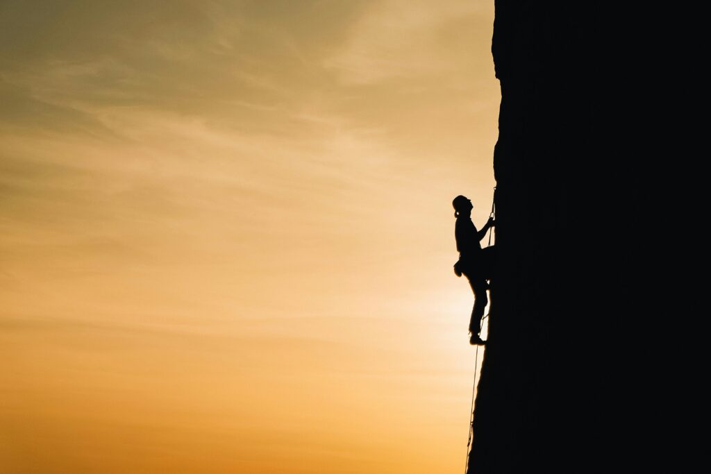 A silhouette of a rock climber scaling a steep cliff during sunset in Russia, showcasing determination and adventure.