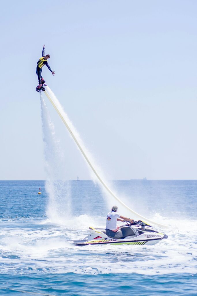 Thrilling flyboarding action as a man performs a high stunt over the sea with a jet ski nearby.