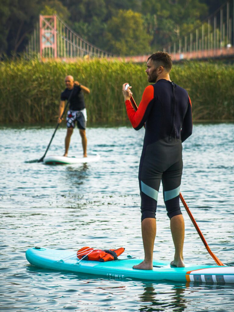 Two men enjoying paddleboarding on a calm lake in nature.