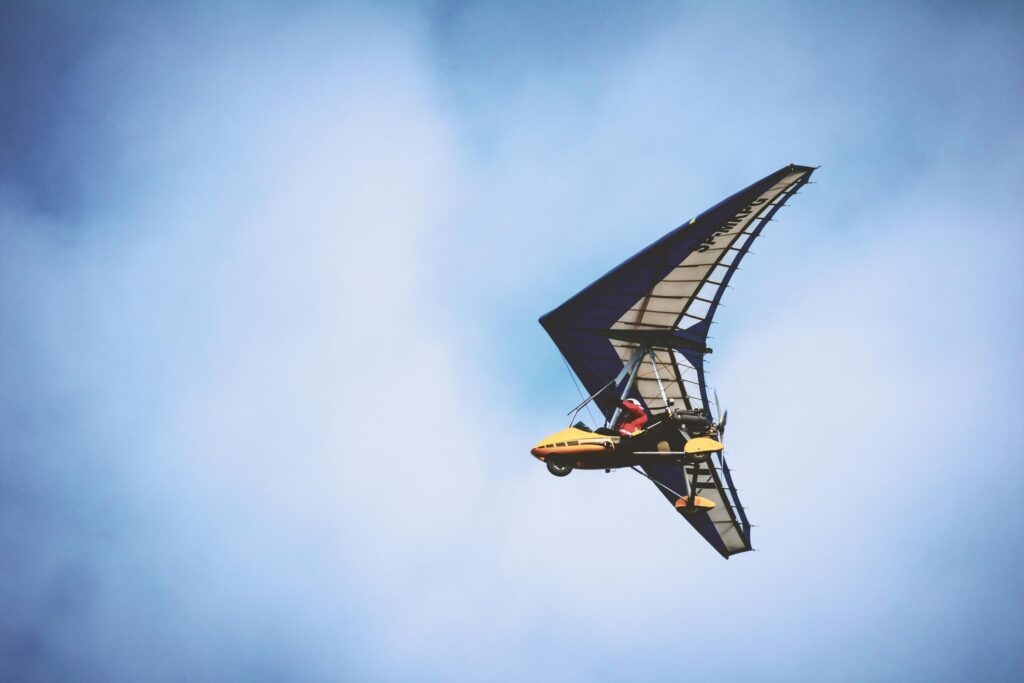 Capture of a powered hang glider soaring through a clear blue sky with a pilot on board.