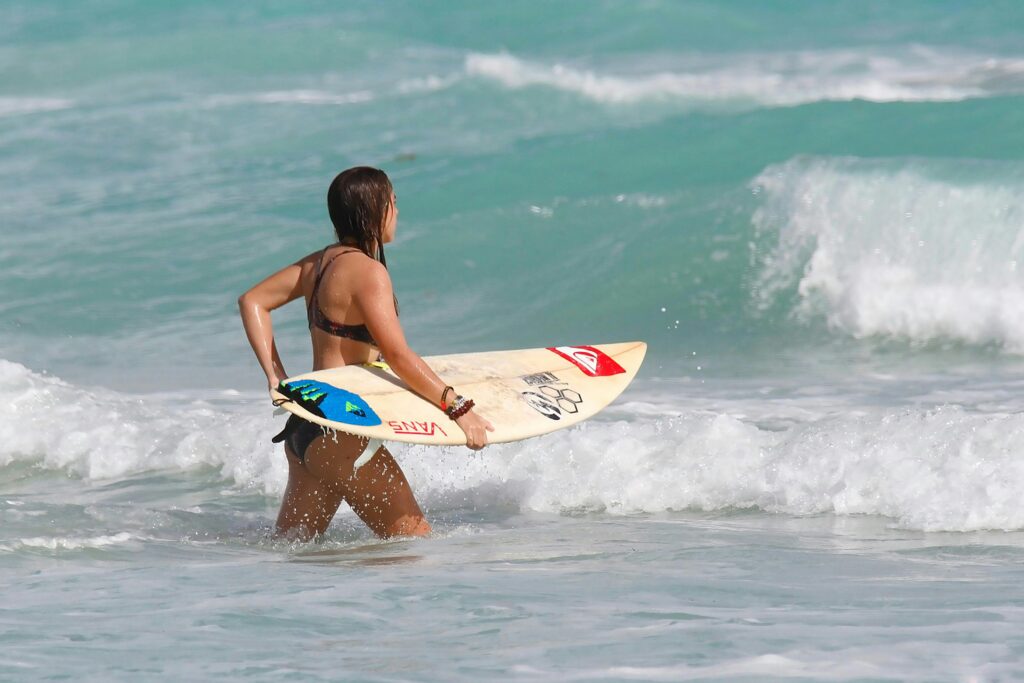 Woman entering the ocean with a surfboard ready to catch some waves under the sunny summer sky.