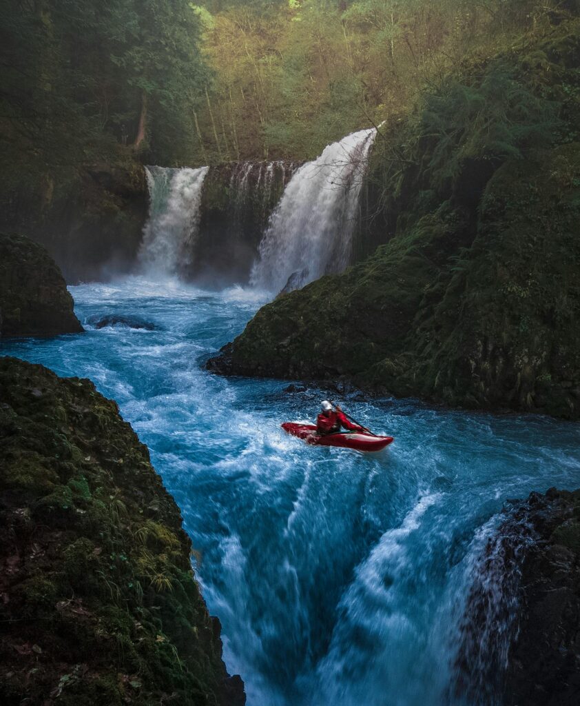 Dramatic scene of a man kayaking down waterfall surrounded by lush forest.