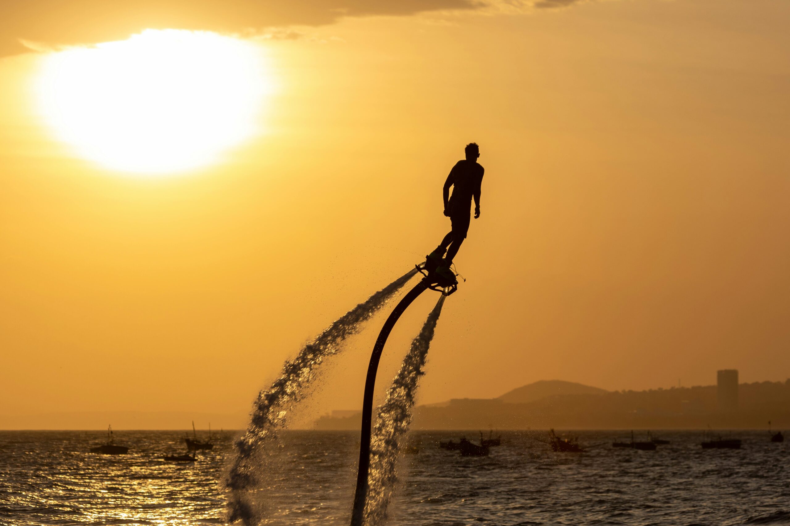 Silhouette of a man flyboarding against a stunning sunset over the sea.