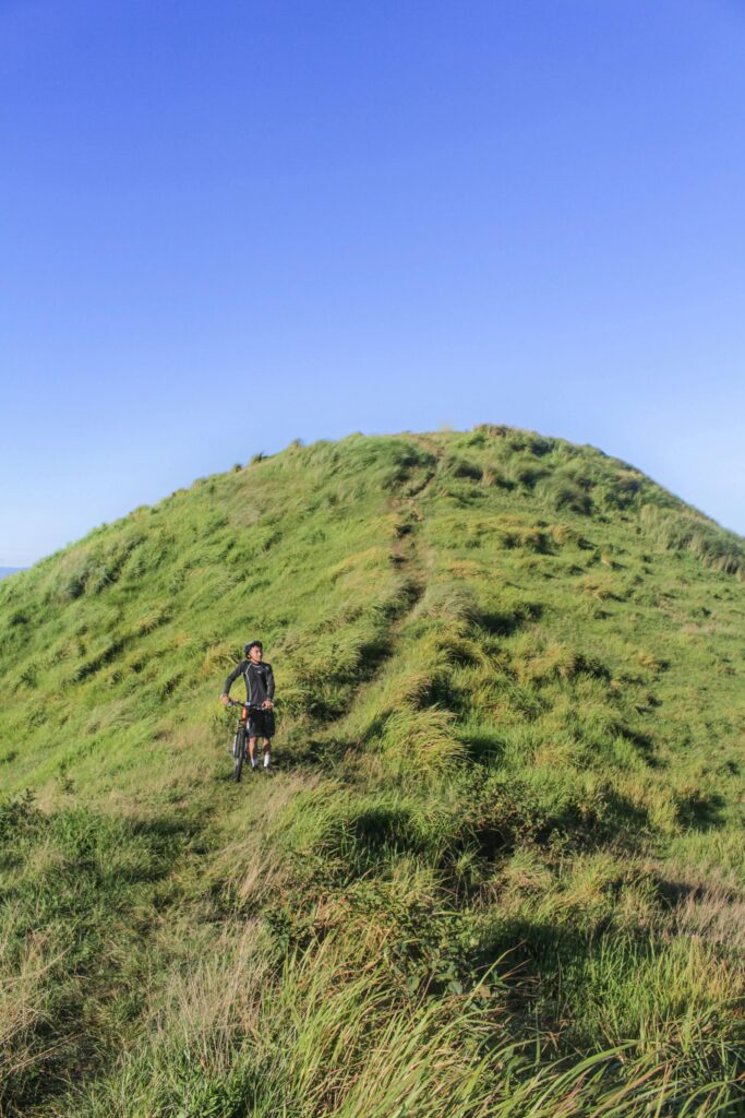 A lone cyclist with mountain bike on a grassy hill; clear blue sky enhances the outdoor adventure vibe.