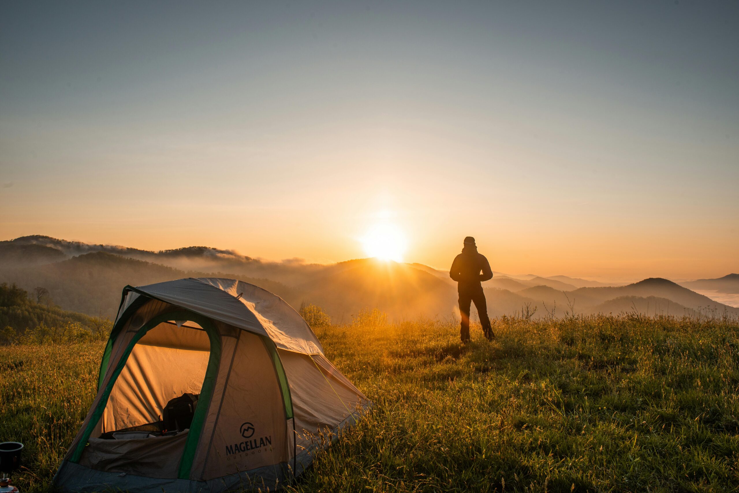 A camper enjoys the sunrise in a mountain setting with a tent. Perfect nature escape.