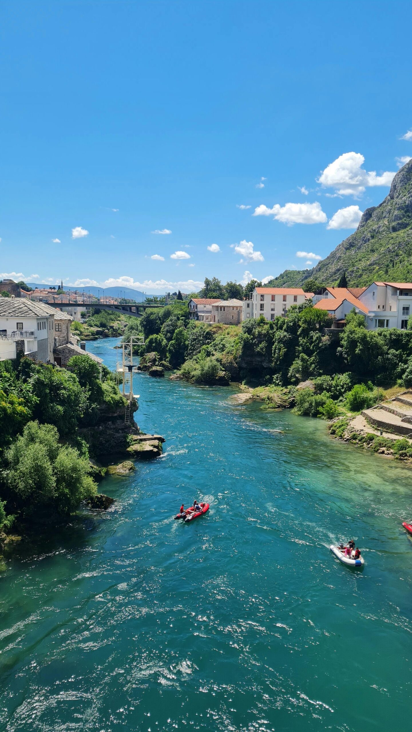 A vibrant scene of kayaks on the Neretva River with lush greenery and mountains in Mostar.