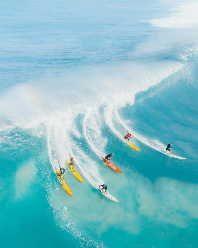 Dynamic aerial photo capturing surfers conquering massive waves in vibrant blue Hawaiian waters.