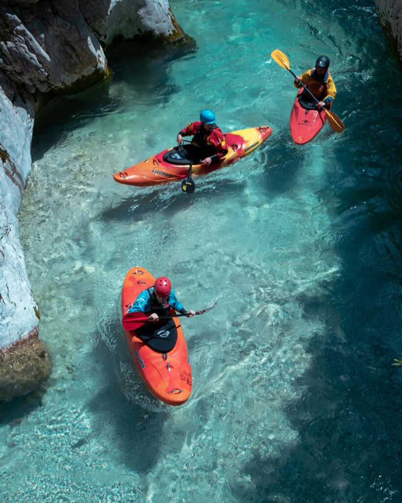 Three kayakers paddle through the stunning clear waters of the Soča River in Slovenia, showcasing adventure and nature.