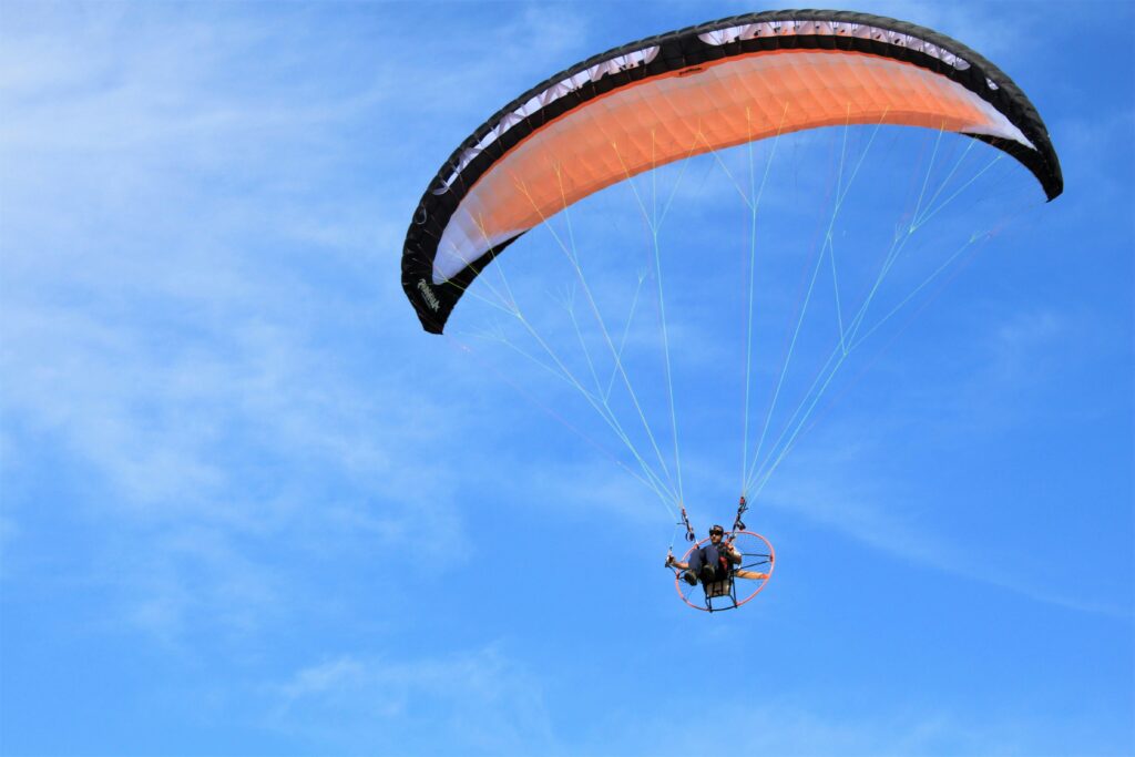 A thrilling view of a paraglider soaring high against a clear blue sky, capturing the essence of adventure sports.