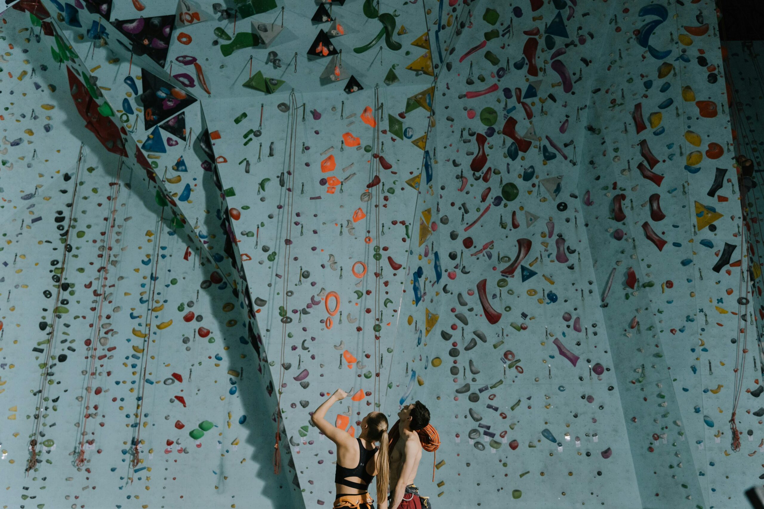 A couple engages in indoor rock climbing, exploring vibrant holds.