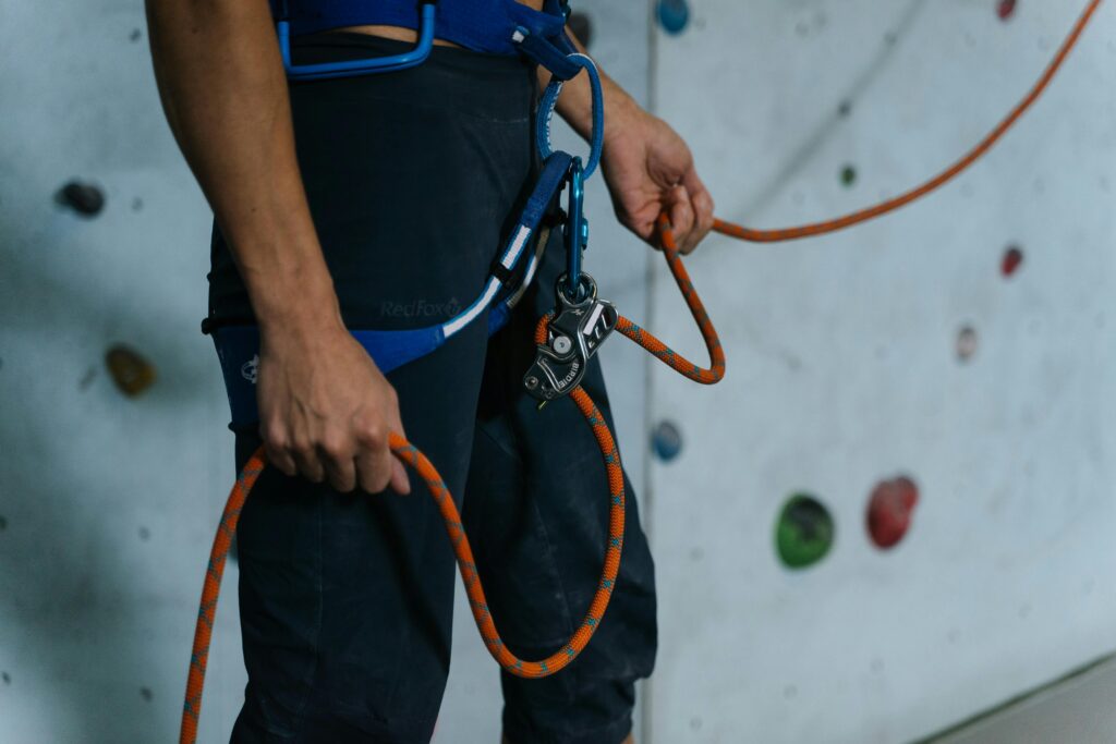 Close-up of climber securing harness with carabiner and rope on indoor wall.