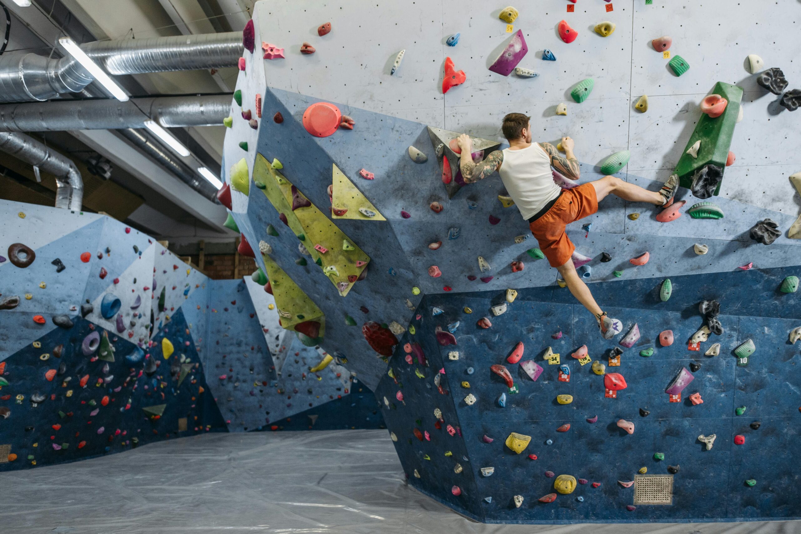 Man bouldering on colorful indoor climbing wall, showcasing athletic skills.