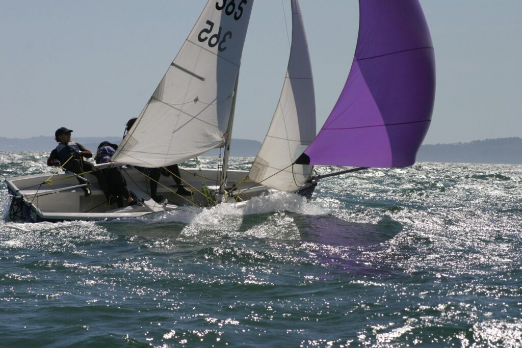 Two sailors navigate a sailboat with colorful spinnaker on a sunny ocean day.