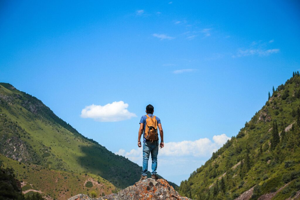 A solo backpacker standing on a rock, admiring the mountain view under a bright blue sky.