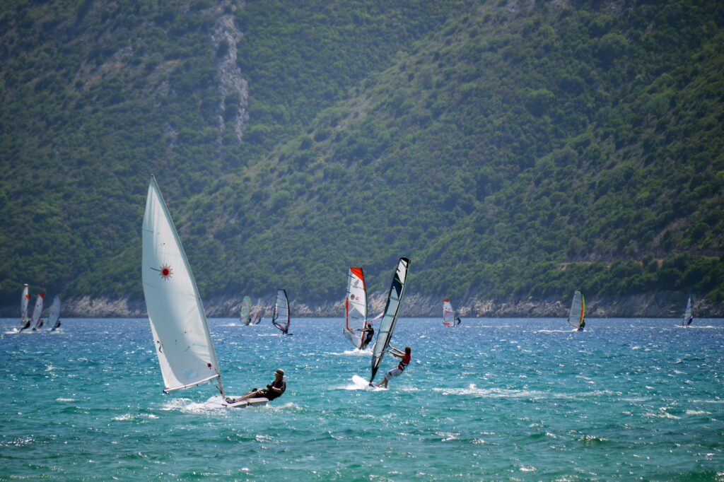 Sailboats and windsurfers enjoy a sunny day on Vasiliki Bay, Greece with lush hills in the background.