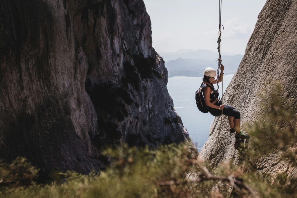 Woman rappelling down a cliff in Sardinia, Italy, showcasing outdoor adventure and thrill.